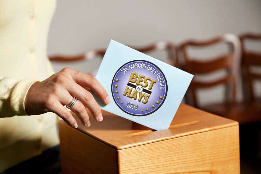 A hand inserting a blue envelope into a wooden ballot box, featuring a circular seal that reads "Best of Hays 2025" and "San Marcos Daily Record."