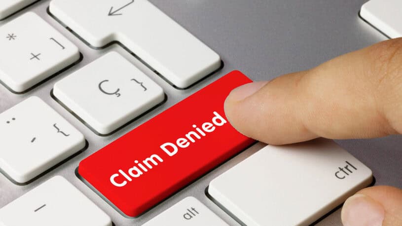 A close-up of a computer keyboard featuring a large red key labelled "Claim Denied," with a finger pressing down on it.